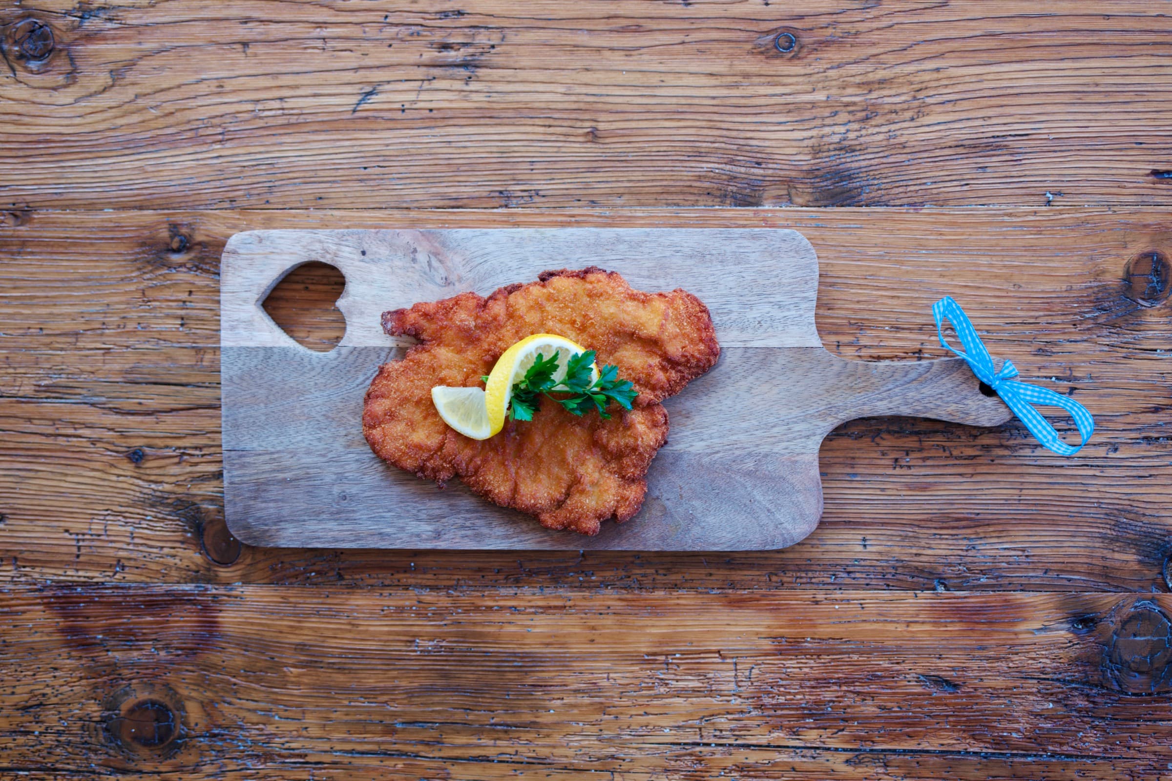 Golden hand-breaded pork schnitzel on a rustic wooden board with lemon and parsley